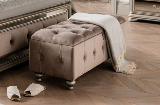 lavish_ Elegant Jessica storage ottoman with a gray throw blanket and a pair of slippers on a wooden floor.