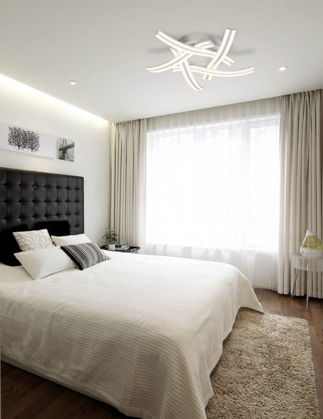 lavish_ A modern bedroom with a large bed featuring elegant Southport furniture, white bedding, the Harvey 5 Light Ceiling, and neutral color scheme.