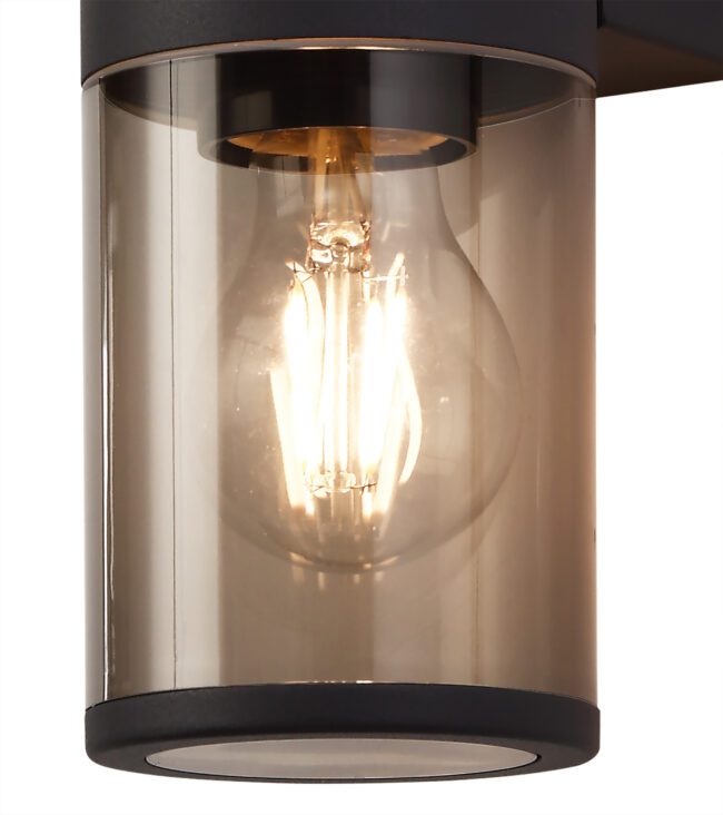 lavish_ The Leo Wall Lamp, an illuminated filament bulb encased within a clear cylindrical lampshade and mounted on a metal base, is perfect for Southport home decor.
