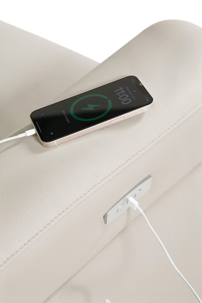 lavish_ A smartphone displaying its charging status resting on a beige surface with a charging cable connected, perfectly blending with the interior design.