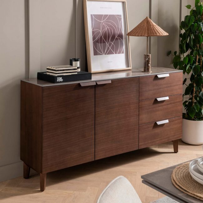 lavish_ A modern Axton Sideboard Latte with drawers in a living room, accessorized with a framed picture, a lamp, and a few small decorative items.